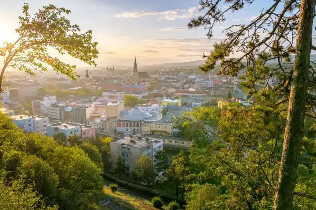 Cluj cityscape viewed from the hills, showcasing urban architecture and lush greenery during sunset.