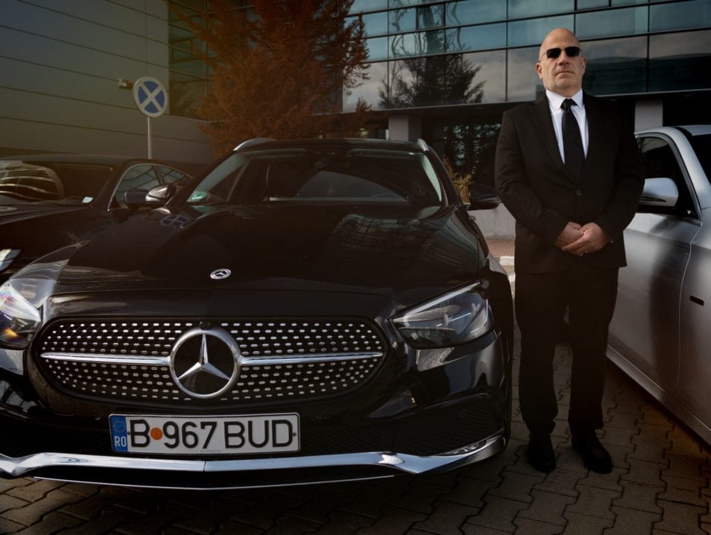 Professional chauffeur beside a black Mercedes E-Class from the Bud’s Cab fleet