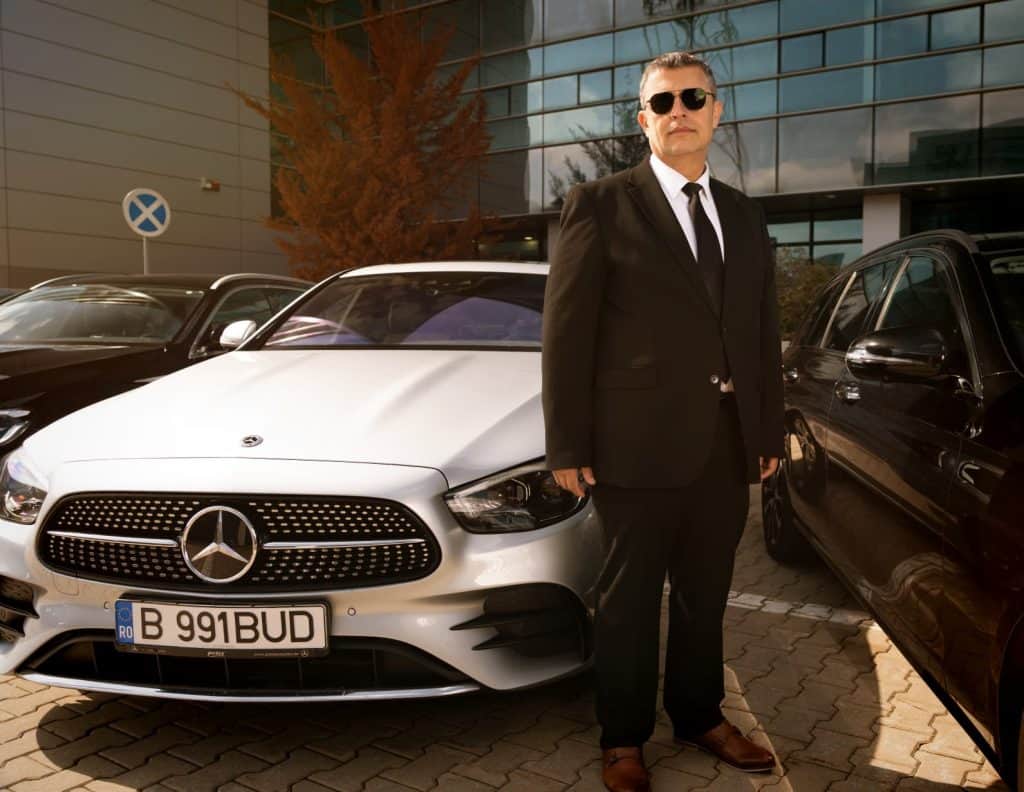 Professional chauffeur beside a white Mercedes E-Class for premium transfer service in Bucharest