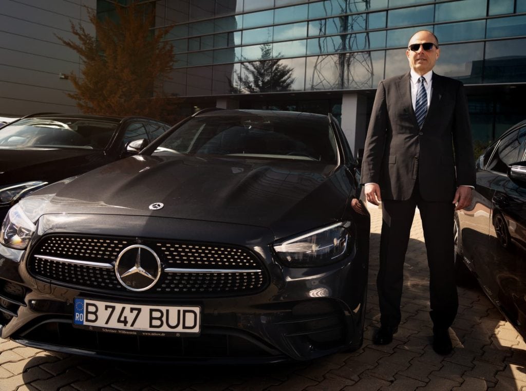 Professional chauffeur standing next to a black Mercedes E-Class from the Bud’s Cab fleet