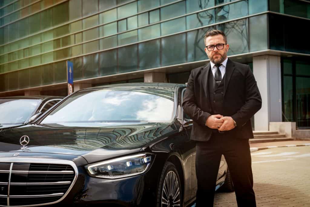 Professional chauffeur standing next to a Mercedes S-Class for luxury transfer service in Bucharest