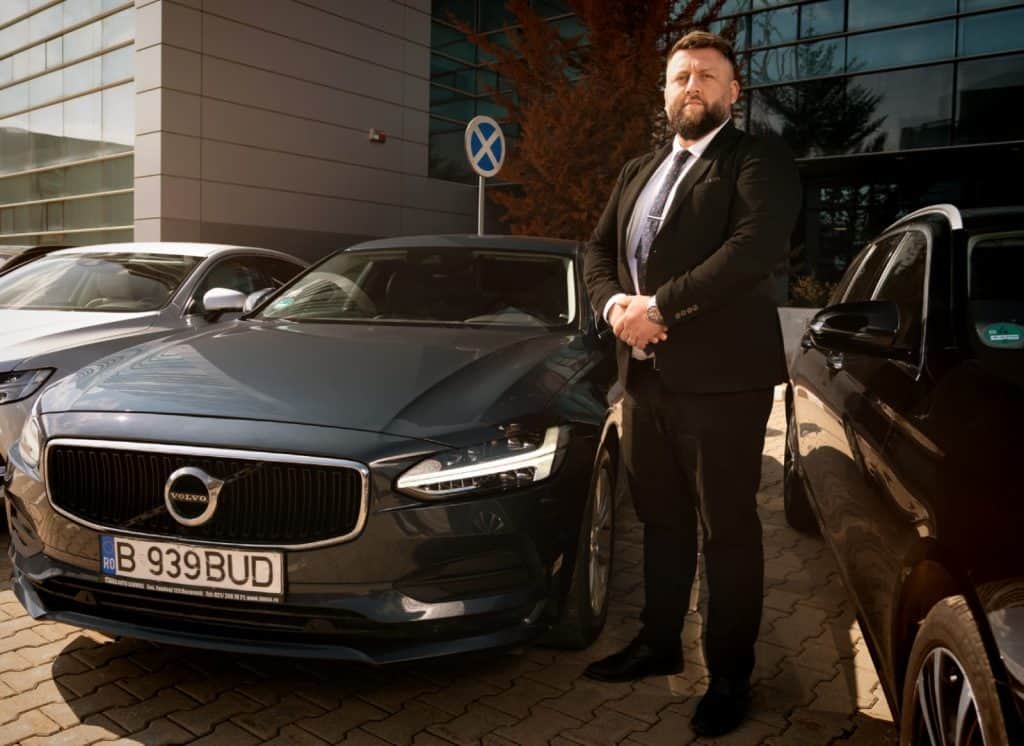 Professional chauffeur standing next to a Volvo S90 from the Bud’s Cab fleet