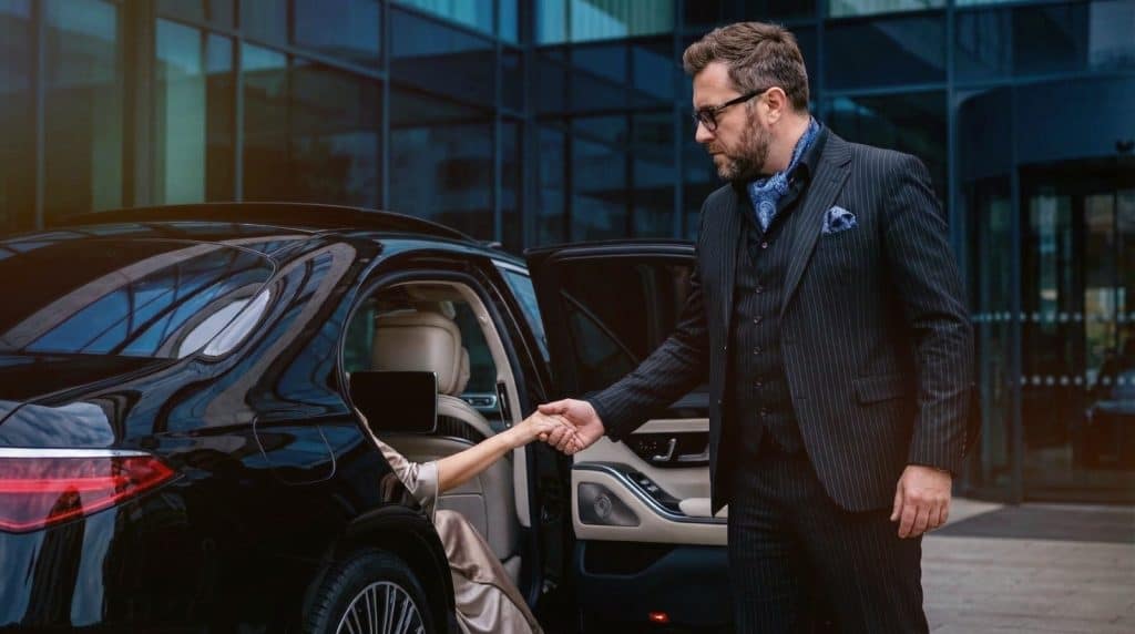 Professional chauffeur helping a VIP passenger exit a black Mercedes S-Class