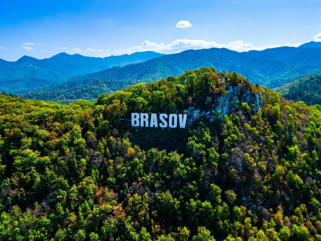 Brasov mountain sign on lush green hillside, scenic landscape for private tours from Bucharest.
