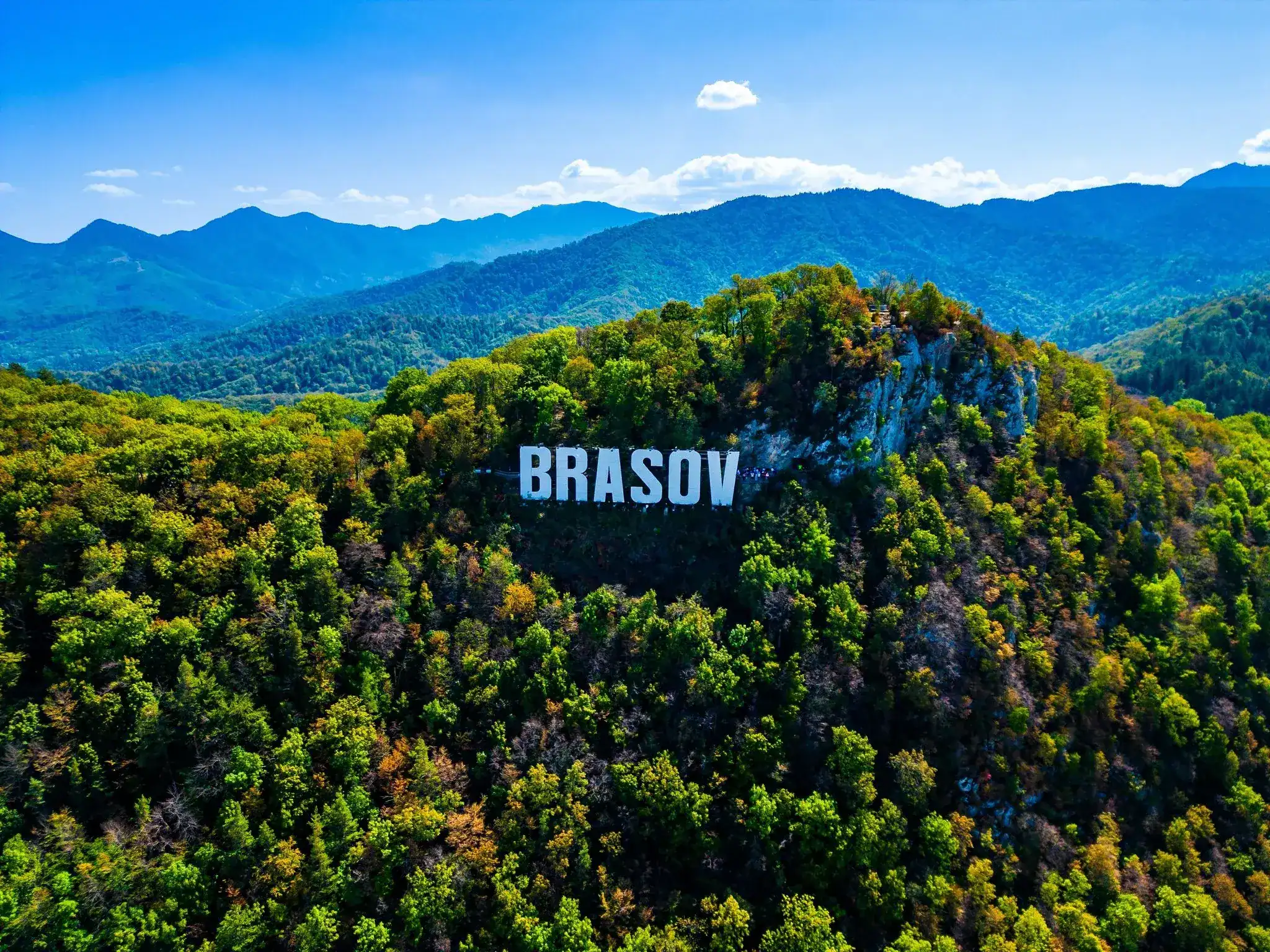 Brasov mountain sign on lush green hillside, scenic landscape for private tours from Bucharest.