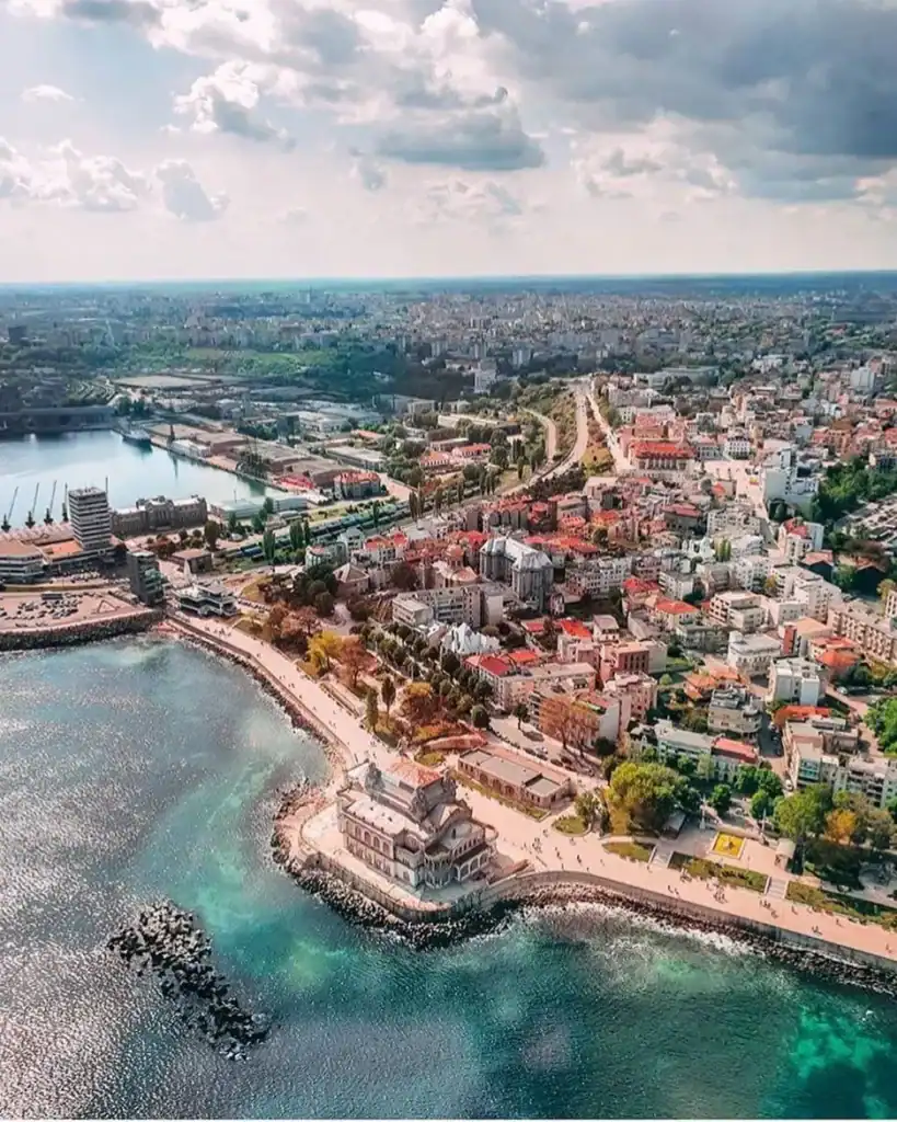 Aerial view of a vibrant coastal city with a mix of modern and historic buildings along the shorelin.