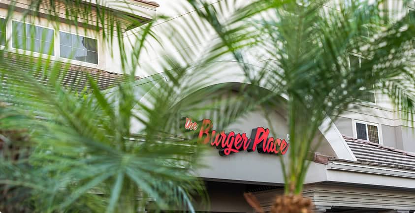 The Burger Place Atlanta storefront sign with lush greenery in the foreground.