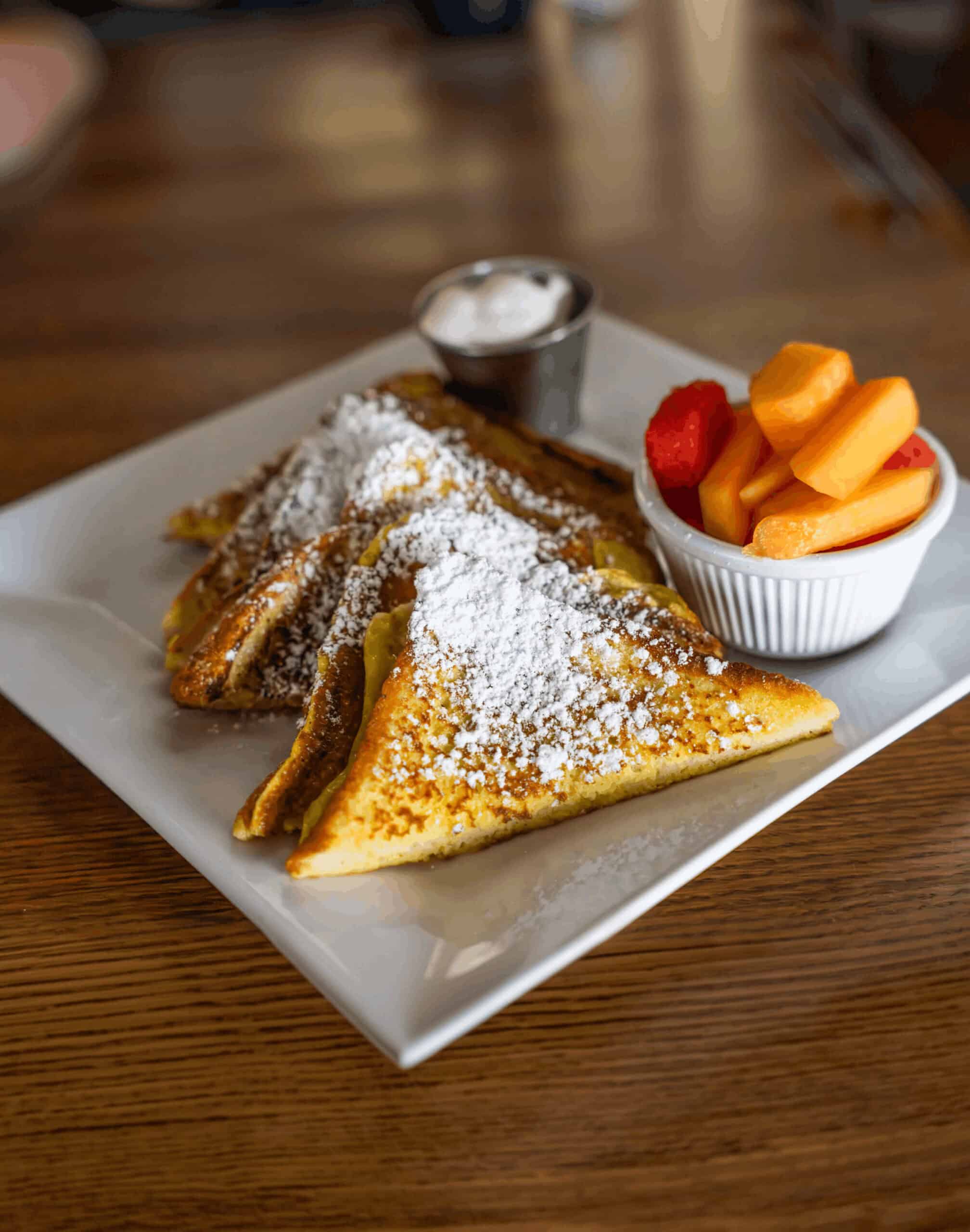 French toast topped with powdered sugar, served with fresh fruit and syrup.