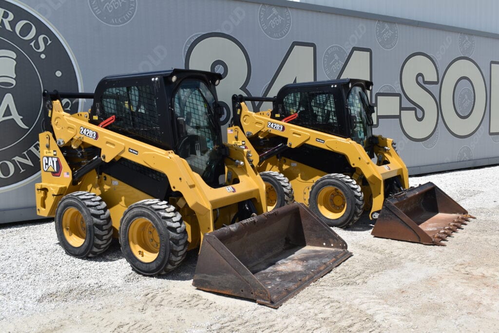 Two yellow CAT compact loaders with buckets at a heavy equipment auction.