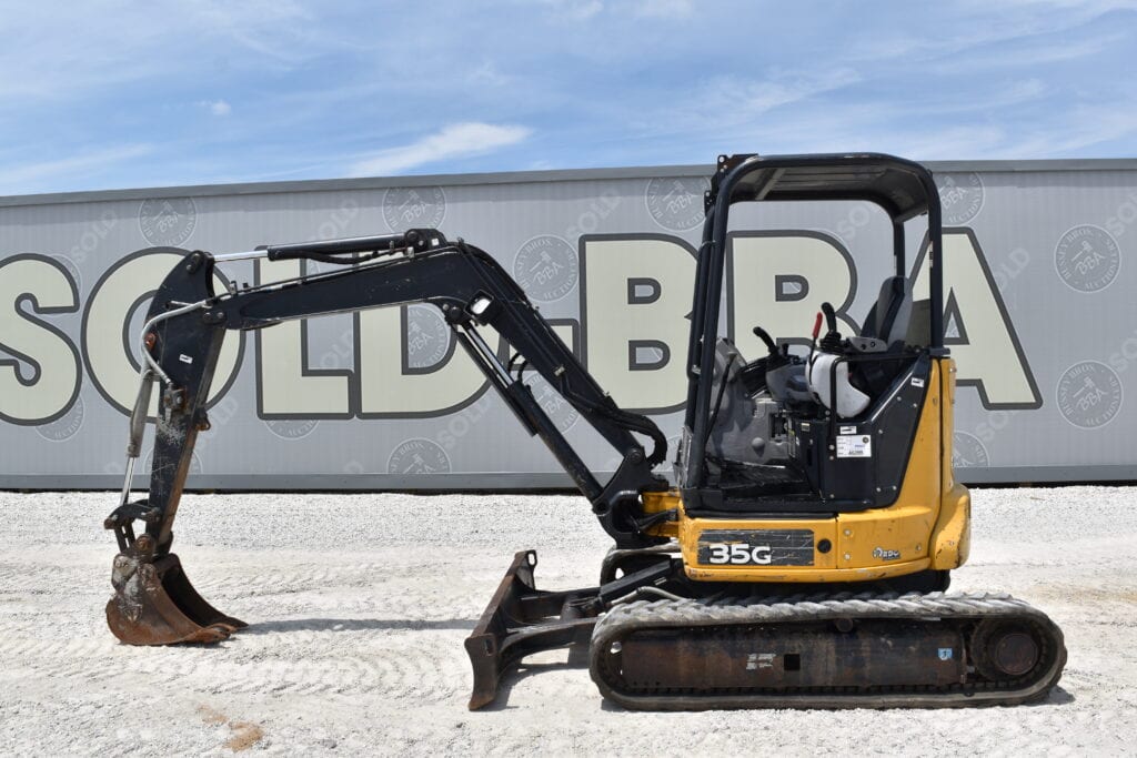Small yellow and black mini excavator on gravel at auction site.