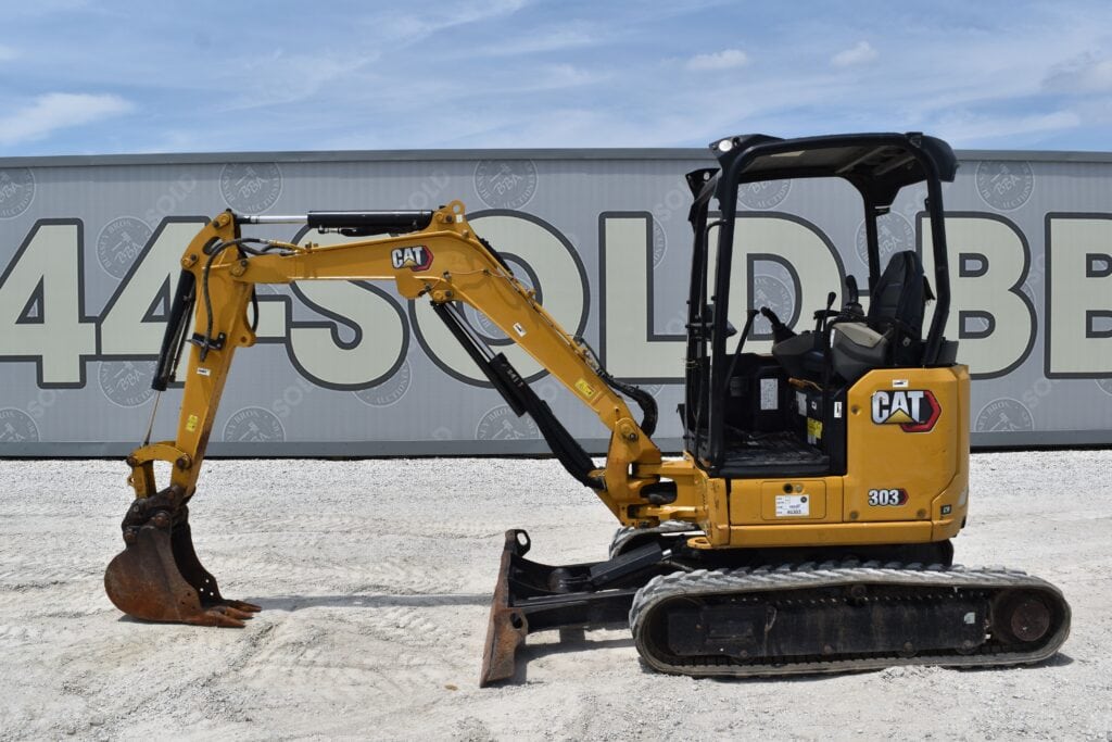 Yellow Caterpillar 303 mini excavator on gravel at auction site.