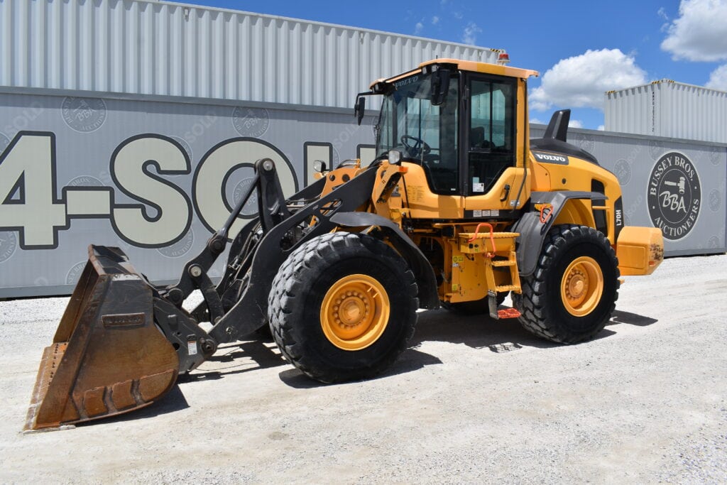 Yellow front loader at Bussey Bros auction site under blue sky.