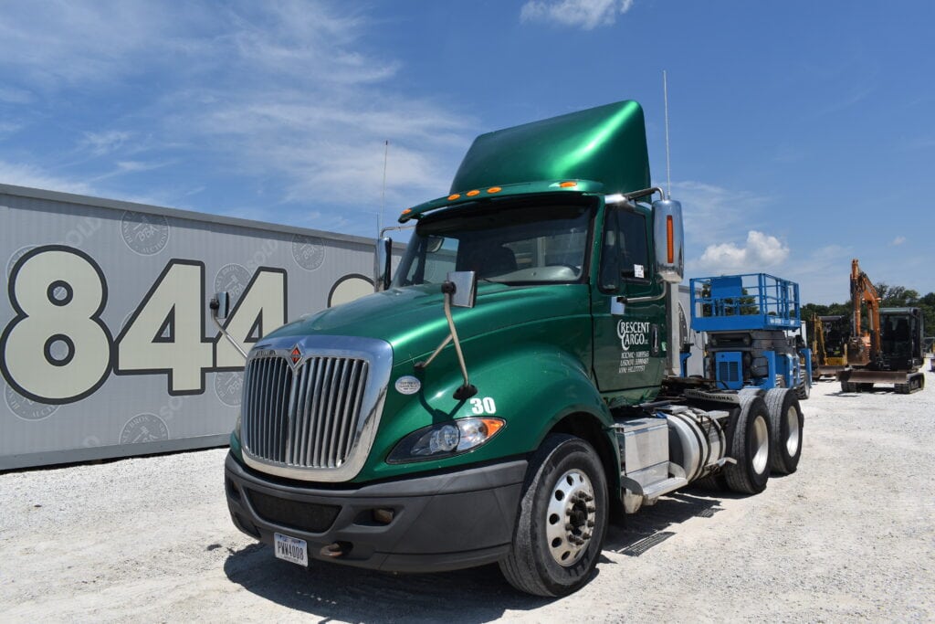 Green semi-truck at heavy equipment auction site.