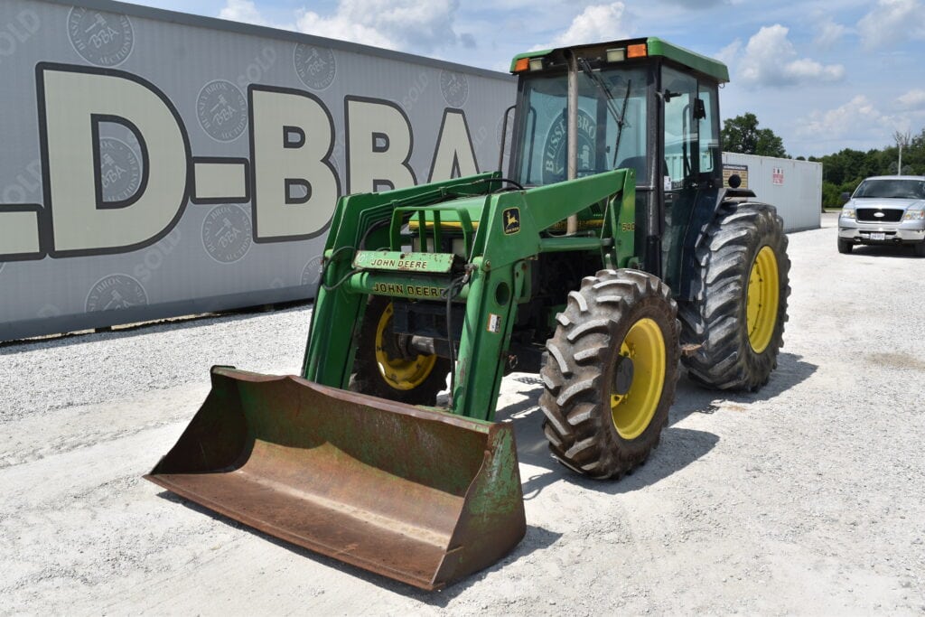 Green John Deere tractor with front loader at auction site.