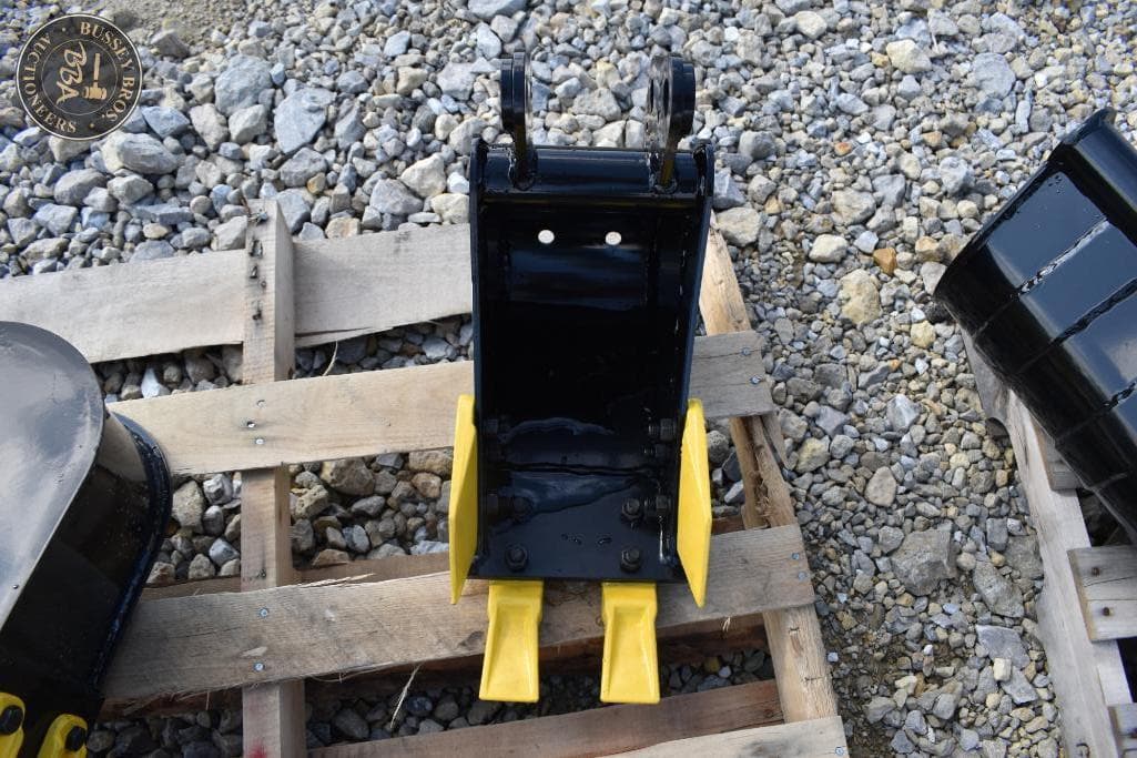 Heavy machinery attachment with yellow and black components on gravel surface.