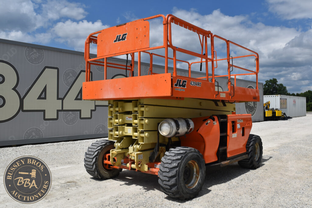 Orange JLG scissor lift on auction lot with blue sky background.