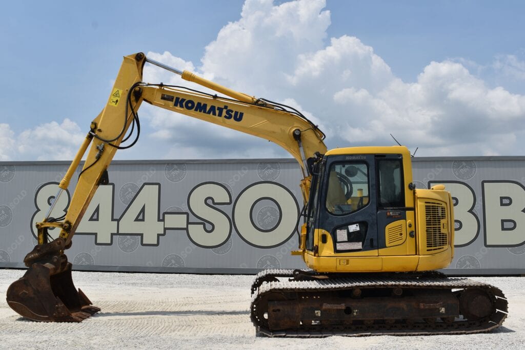 Yellow Komatsu mini excavator on auction lot with cloudy sky.