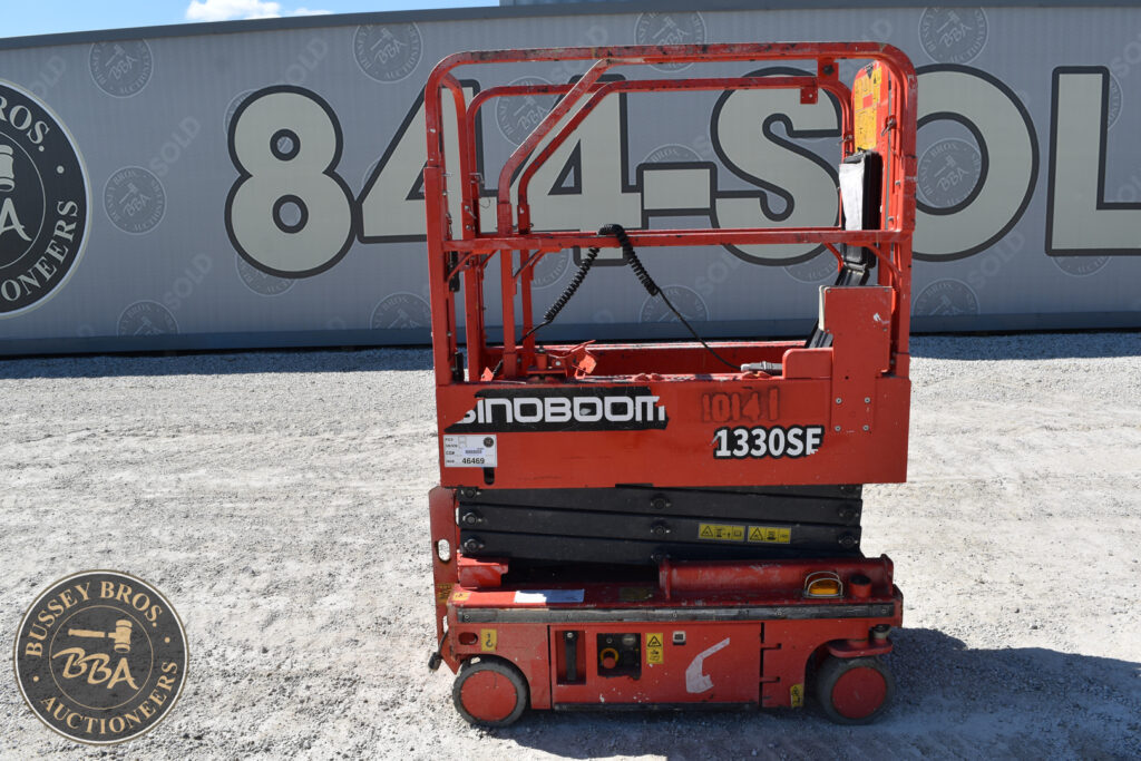 Red electric scissor lift at heavy equipment auction site.