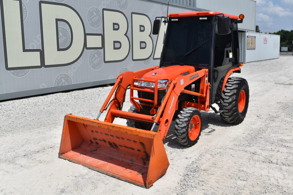 Compact orange tractor with front loader at auction site.
