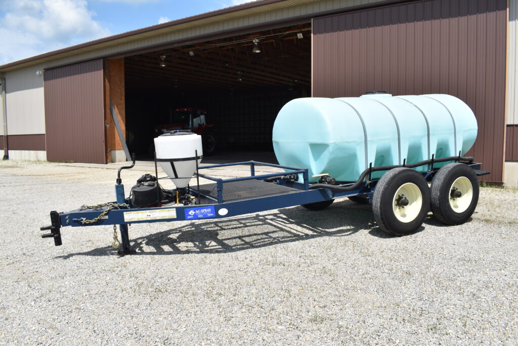 Farm water tank trailer with dual wheels and pump system outside barn.