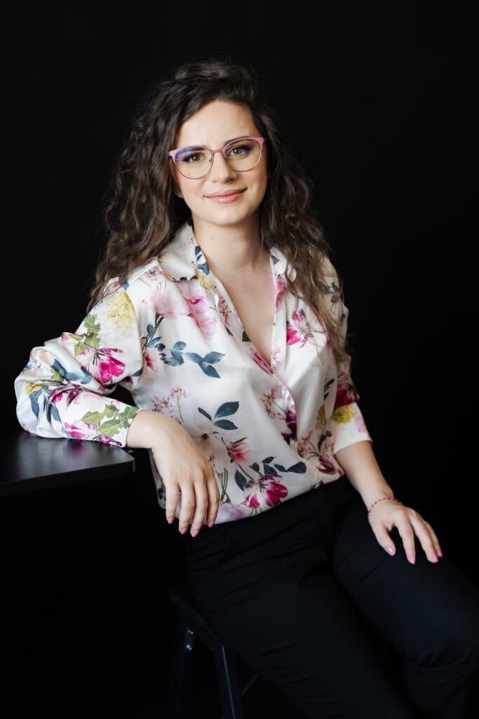 Alb negru, portret femeie cu ochelari roz și bluză florală albă, reprezentând profesionalism și creativitate în domeniul tehnologiei, ideal pentru site-uri de tehnologie sau branding profesional.