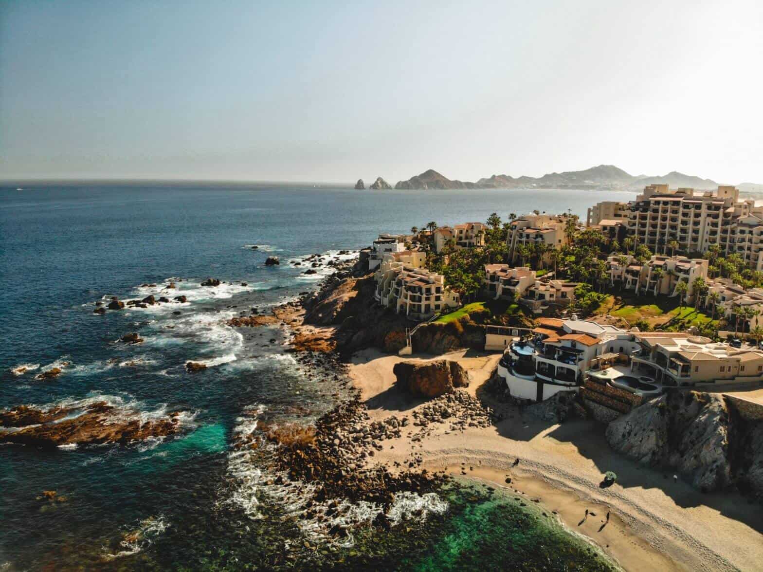 Is Cabo San Lucas Safe? What Cabo Bello Visitors And Homeowners Should Know – Homes For Sale In Cabo Bello Drone Shot Of Luxury Villas Built Along The Rocky Coastline Of Cabo San Lucas, With The Ocean And Hills In The Background.