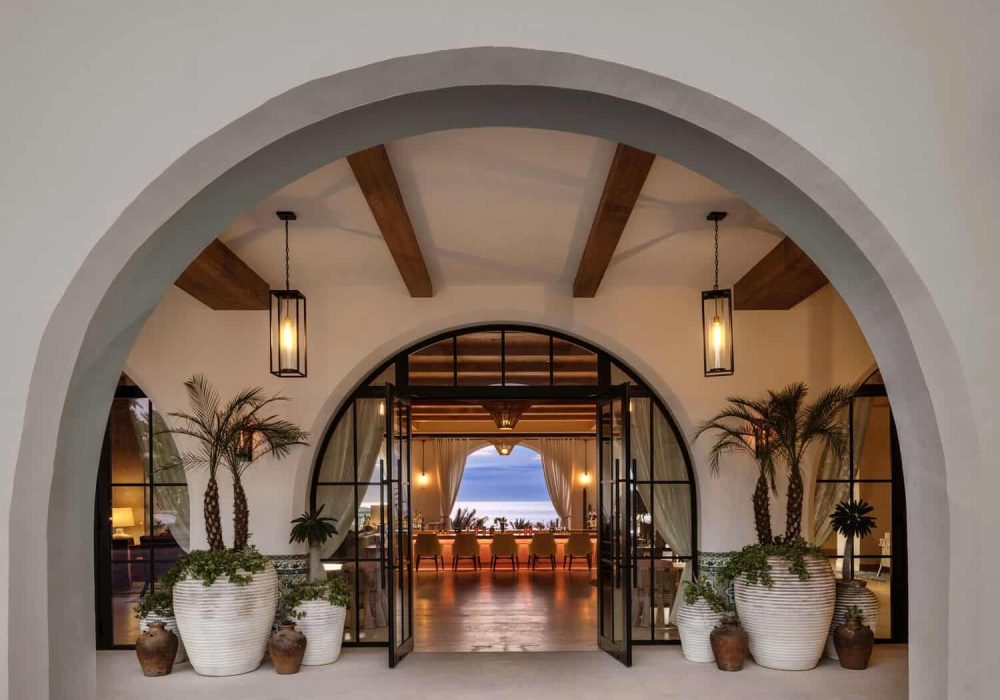 Luxury Modern Villa Entrance With Elegant Arches, Potted Palm Trees, Ambient Lighting, And Panoramic Ocean View, Showcasing Premium Cabo Del Sol Real Estate In Mexico.
