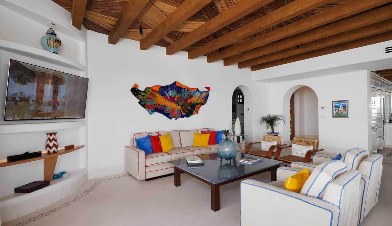 "Spacious living room at Las Ventanas PH 6502 featuring custom wood-beam ceiling, modern decor, flat-screen TV, and cozy seating with vibrant accent pillows."