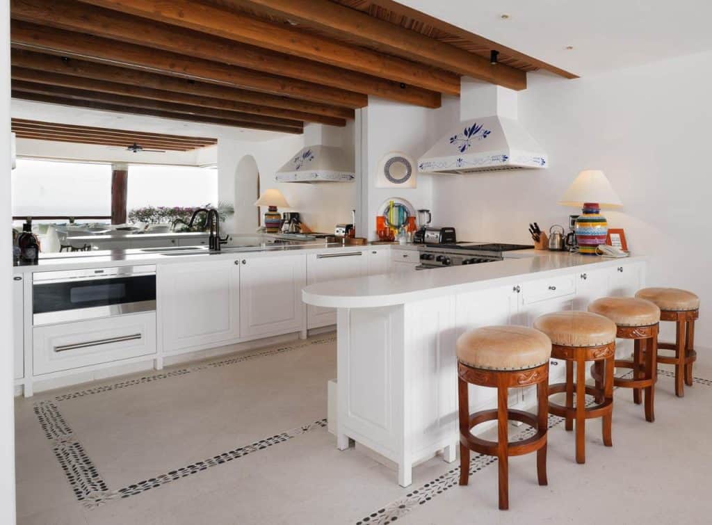 Spacious white gourmet kitchen with wooden beams, large island, breakfast bar seating, and premium appliances at Las Ventanas PH6502, Cabo Real Corridor.