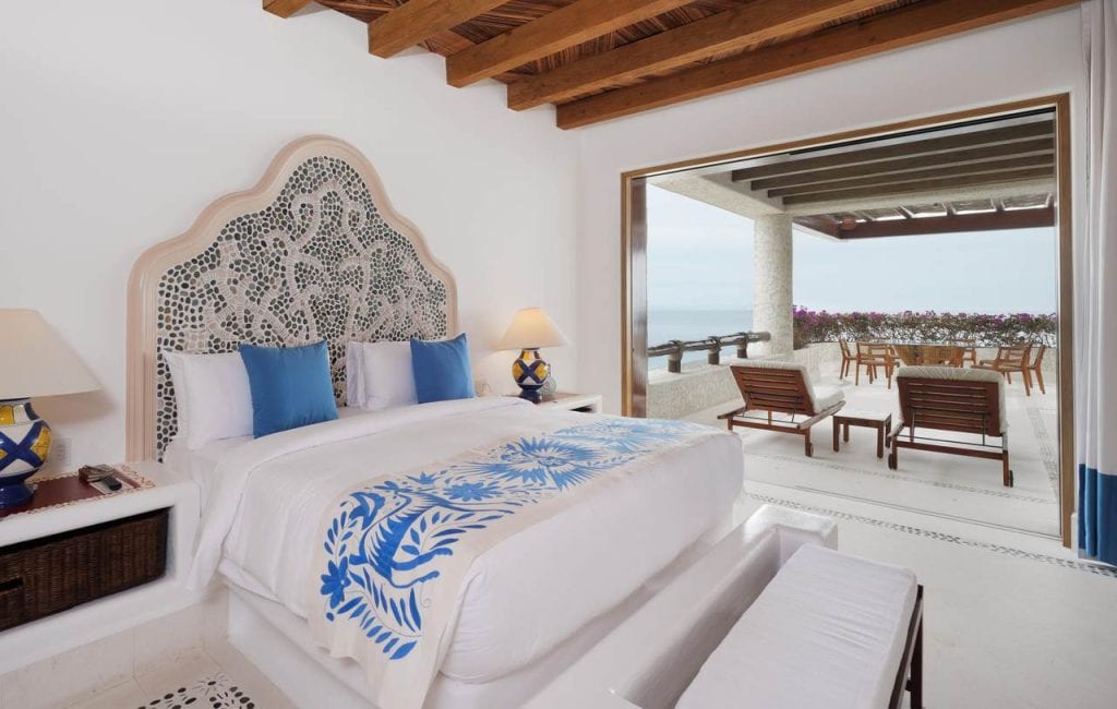 Luxury master bedroom at Las Ventanas PH6502 with custom stone headboard, wood-beam ceiling, ocean views, and direct access to private terrace seating area.
