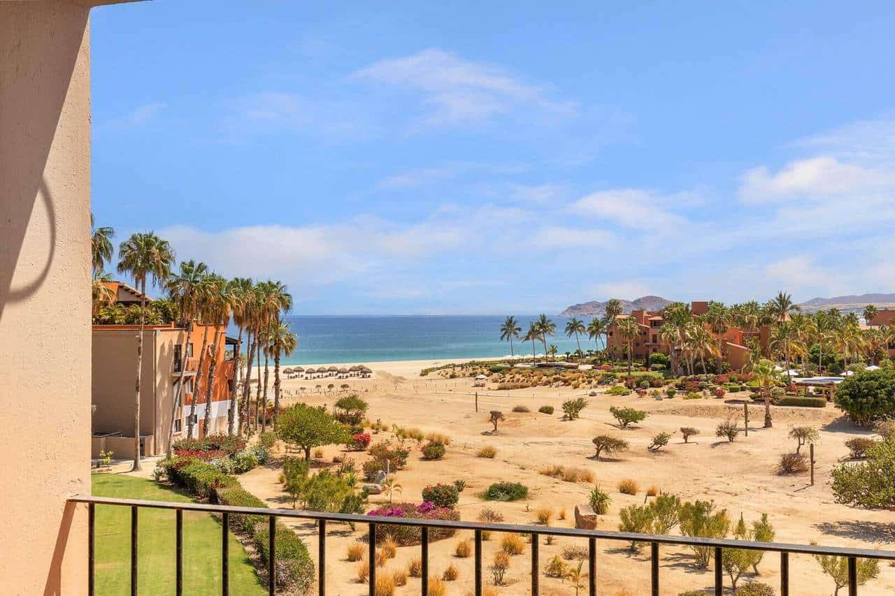 Panoramic View Of Cabo Real Beachfront Property Showing Lush Gardens, Sandy Beach, Clear Blue Ocean, And Palm Trees, Highlighting Luxury Cabo Real Real Estate Opportunities With Breathtaking Coastal Scenery.