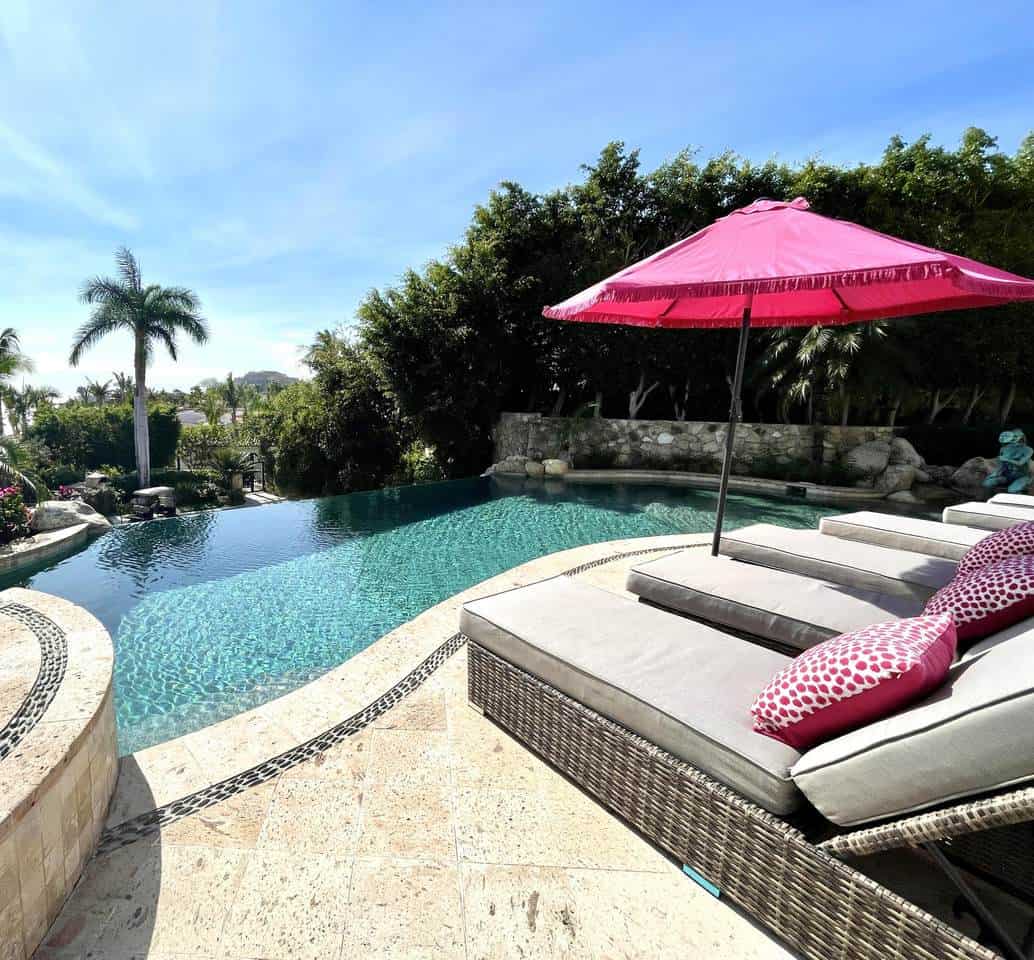 1. Luxurious Cabo Real Estate Pool With Pink Umbrella, Tropical Trees, And Scenic Ocean Views, Perfect For Relaxing.