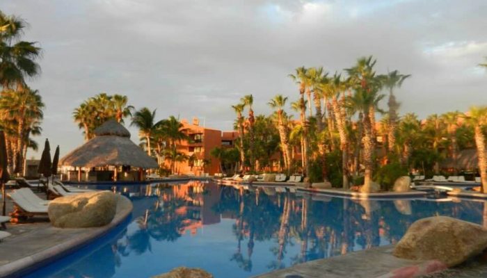 Luxury Resort Pool At Cabo Real Beaches And Pools In Los Cabos, Featuring Palm Trees, Lounge Chairs, And Sunset Reflections Over The Water.