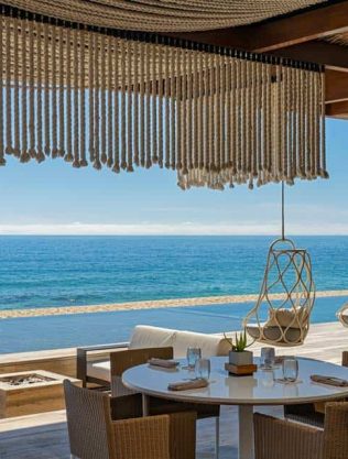Elegant Cabo Real Beachfront Dining Area With Ocean View, Modern Hanging Chairs, And Stylish Décor, Perfect For A Luxurious Seaside Experience In Cabo Real.