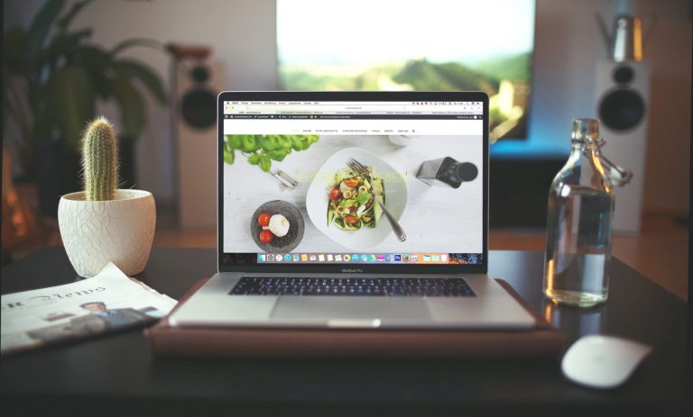 A photograph of a food blog on a laptop. The laptop is sitting on a desk in front of a window.