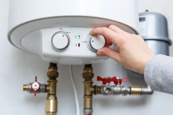 A person adjusts the temperature dial on a wall-mounted water heater, showcasing a recent boiler installation with visible pipes and valves beneath the unit.