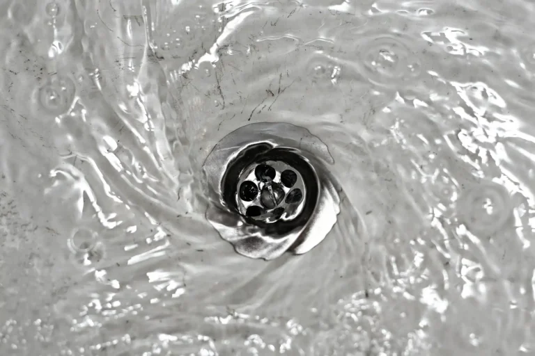 Water swirling down a metal sink drain, creating a vortex with visible ripples and bubbles—a clear sign it might be time to consider a professional Drain Clearing Service.