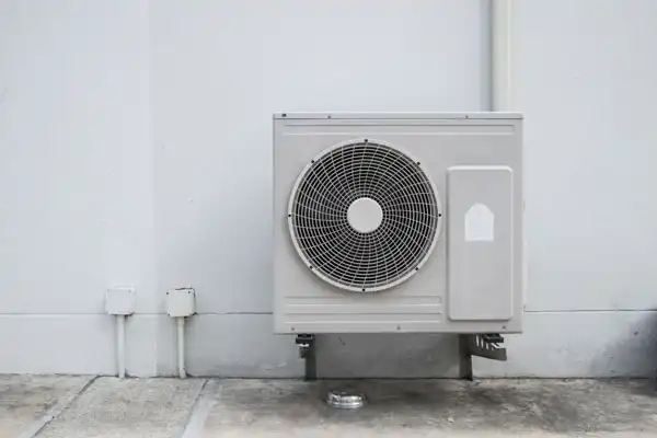 An outdoor heat pump installation mounted on a concrete wall, with visible pipes and electrical boxes situated nearby.
