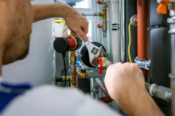 A person uses a wrench to adjust a valve on a network of pipes and fittings, likely performing maintenance, repair, or humidifier installation on plumbing or heating equipment.