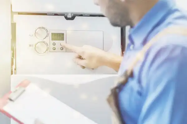 A person in work clothes adjusts the settings on a control panel, holding a clipboard in the other hand during a tankless water heater installation.