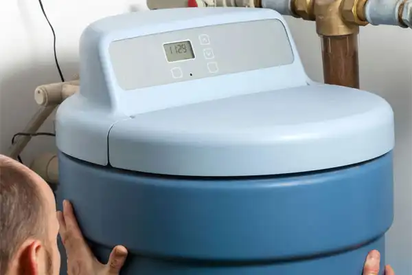 A person adjusts a blue water softener unit with a digital control panel, highlighting a recent water softener installation next to copper pipes.