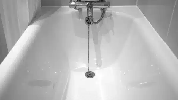 A white bathtub with a metal drain plug attached to a chain, viewed from above with a faucet visible at the far end.