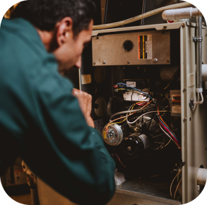A person in a green shirt inspects the internal components and wiring of a furnace or HVAC unit as part of a Hero maintenance plan.