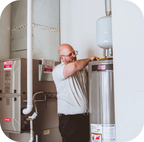 A man adjusts a component on a residential water heater in a utility room with HVAC equipment, showcasing the importance of regular upkeep like the Hero maintenance plan.