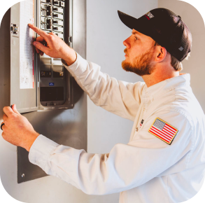 A technician in a uniform and cap checks or operates a circuit breaker panel mounted on a wall as part of the Hero maintenance plan.