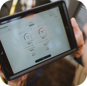 A person holds a tablet displaying numerical data, gauges, and settings, possibly related to system performance or diagnostics as part of a Hero maintenance plan.