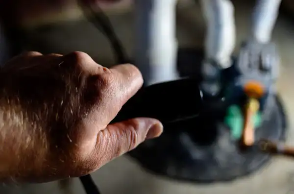 Close-up of a person's hand holding a camera or similar device, focusing on a blurred background with a standing figurine or object.
