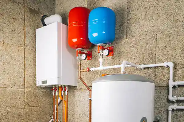A heating system with a white boiler, red and blue expansion tanks, and a cylindrical water heater. It is mounted on a textured wall with visible pipes connected.