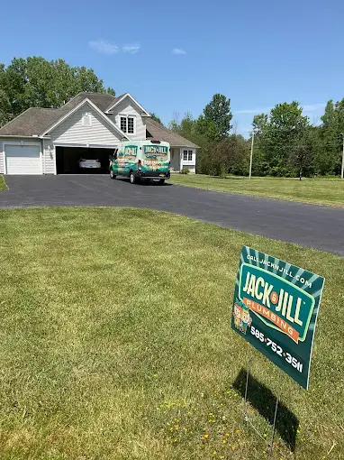 A Jack and Jill Plumbing van is parked in front of a house with a matching service sign on the lawn under a clear blue sky.