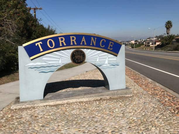 Torrance city entrance sign with blue lettering and decorative waves, located along a roadside in Torrance, CA, representing the local community.